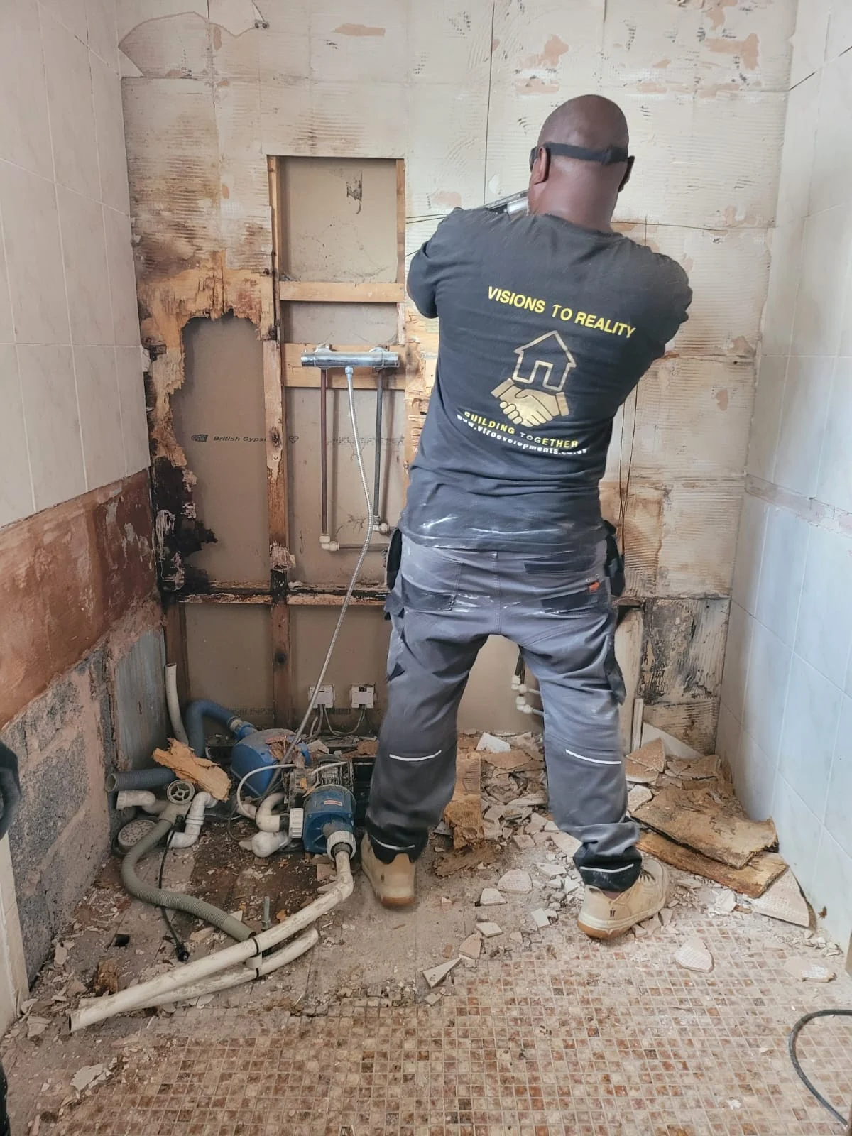 Tradesperson preparing a bathroom wall beside exposed plumbing
