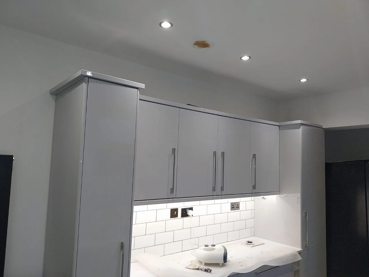 Finished grey kitchen cabinetry and white worktops with ceiling spotlights