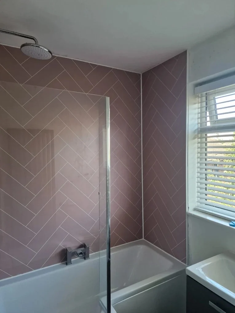 Bath and glass shower screen against pink herringbone wall tiles
